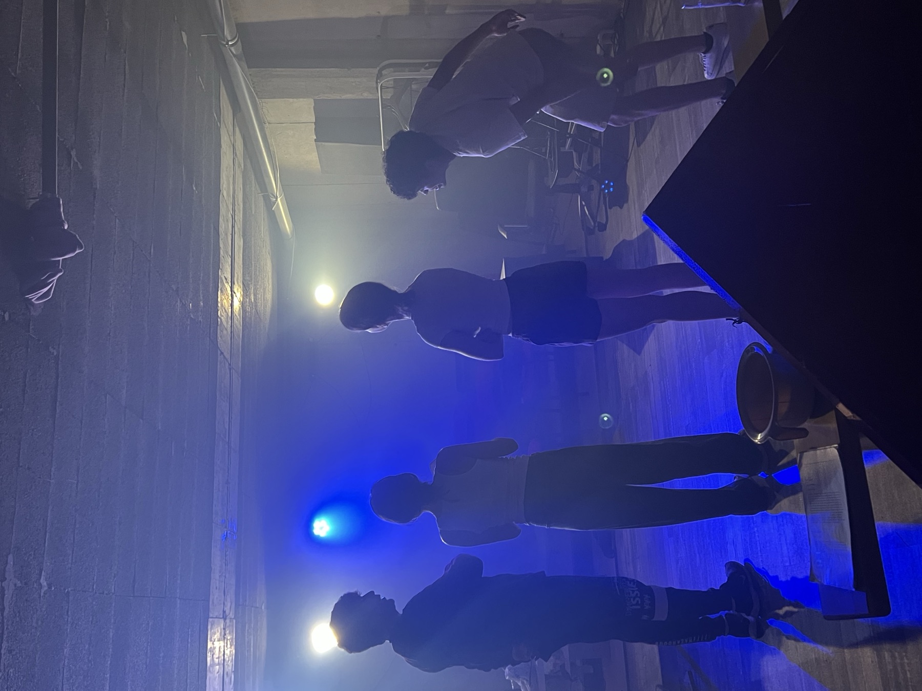 Cuatro alumnos de pie en la sala de Nalda, a contraluz, con niebla y luz azul de escena